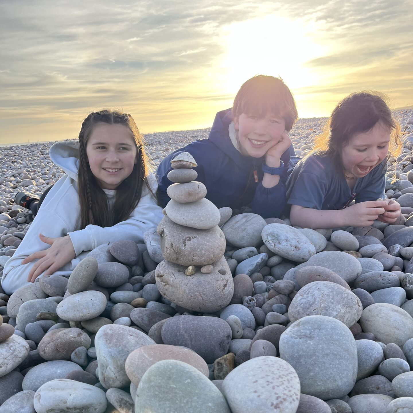 3 kids on a stony beach with a stack of pebbles in front of them