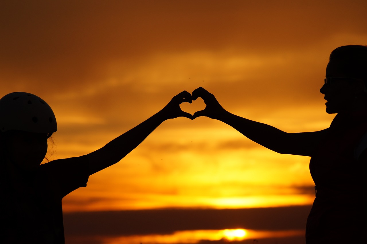 boosting your child's self esteem with 2 people in a sunset holding hands in in the shape of a heart