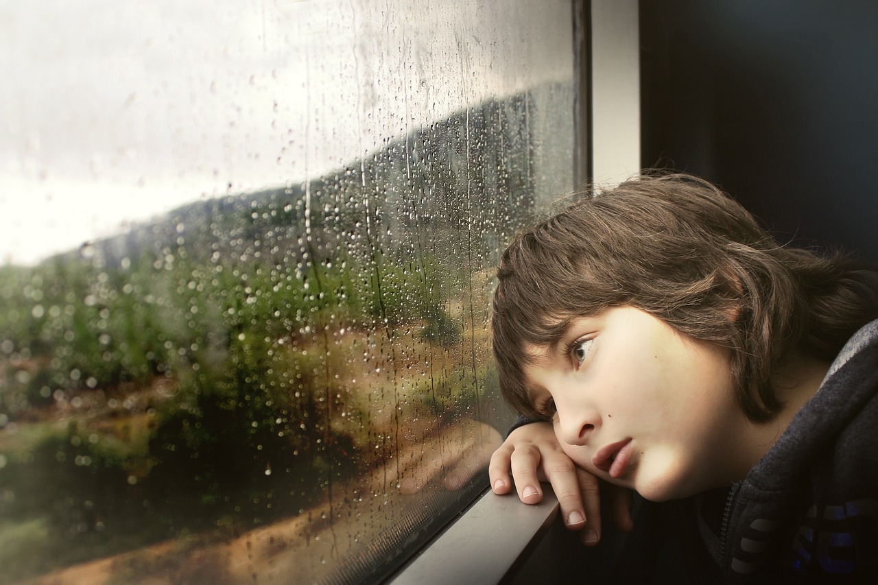 loss of a sibling - a boy looking out of a rainy window
